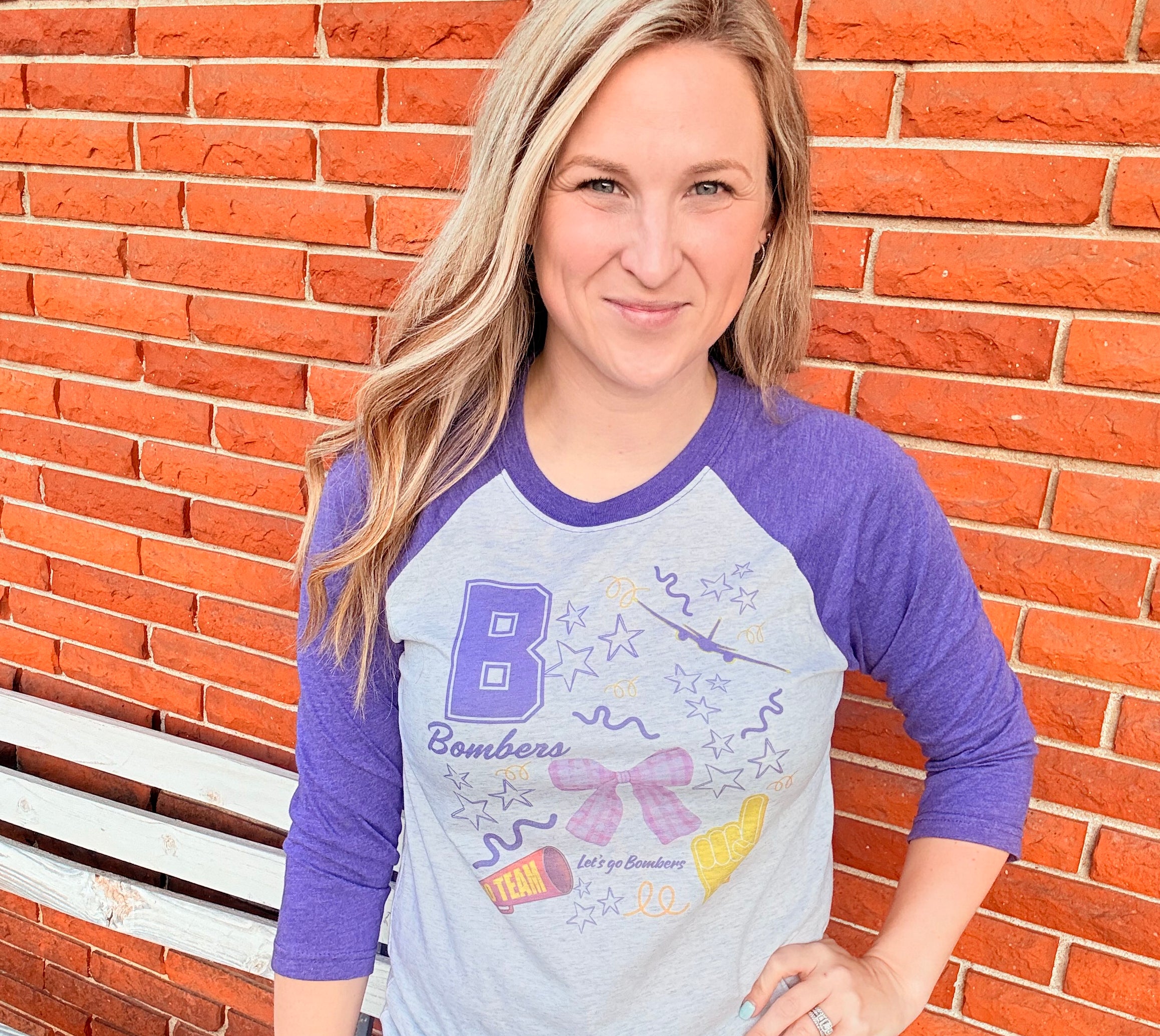 Person wearing a purple and white long-sleeve shirt with a graphic design, sitting on a brick surface.
