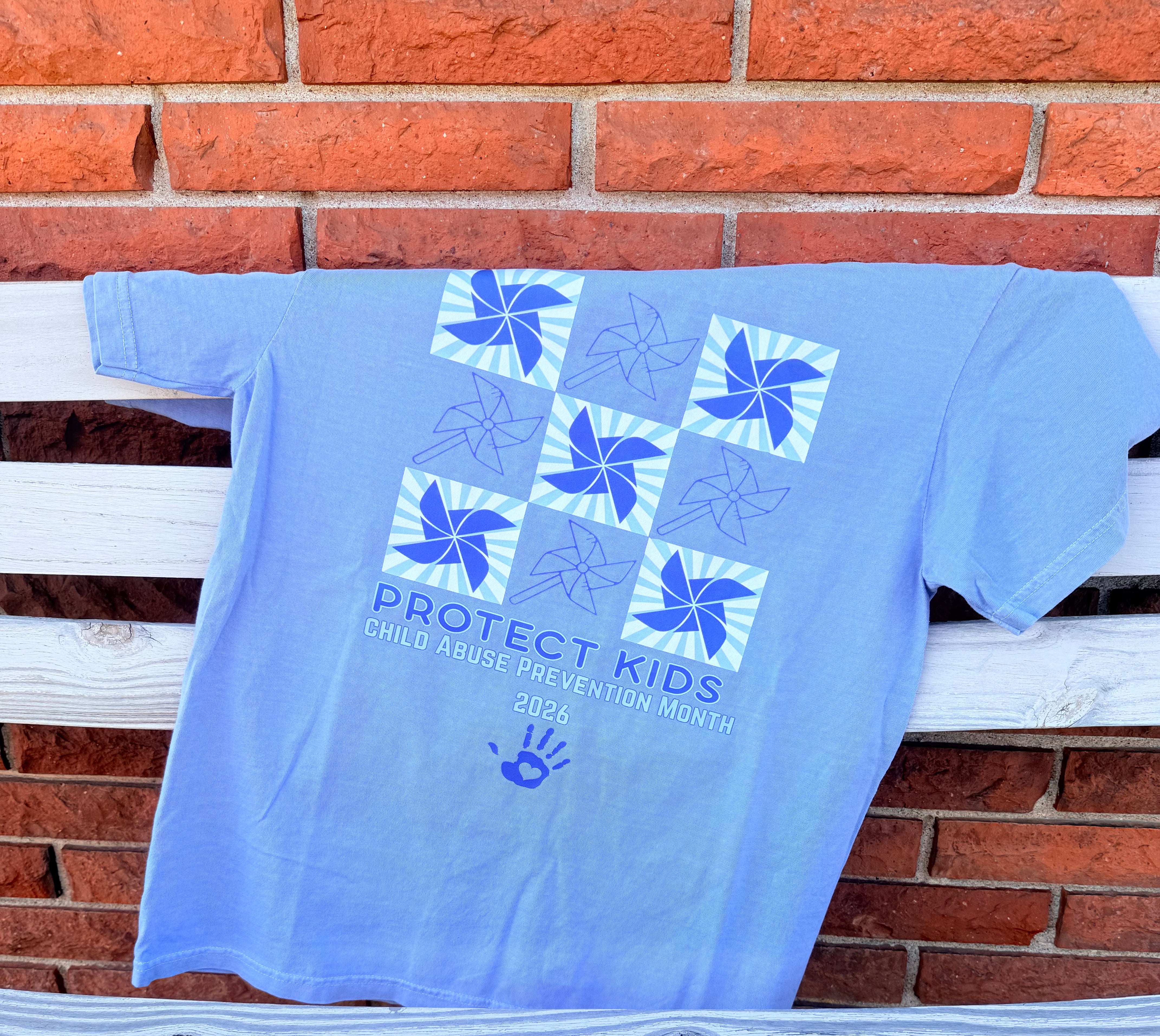 Blue sweatshirt with a logo and text hanging on a clothesline against a brick wall.