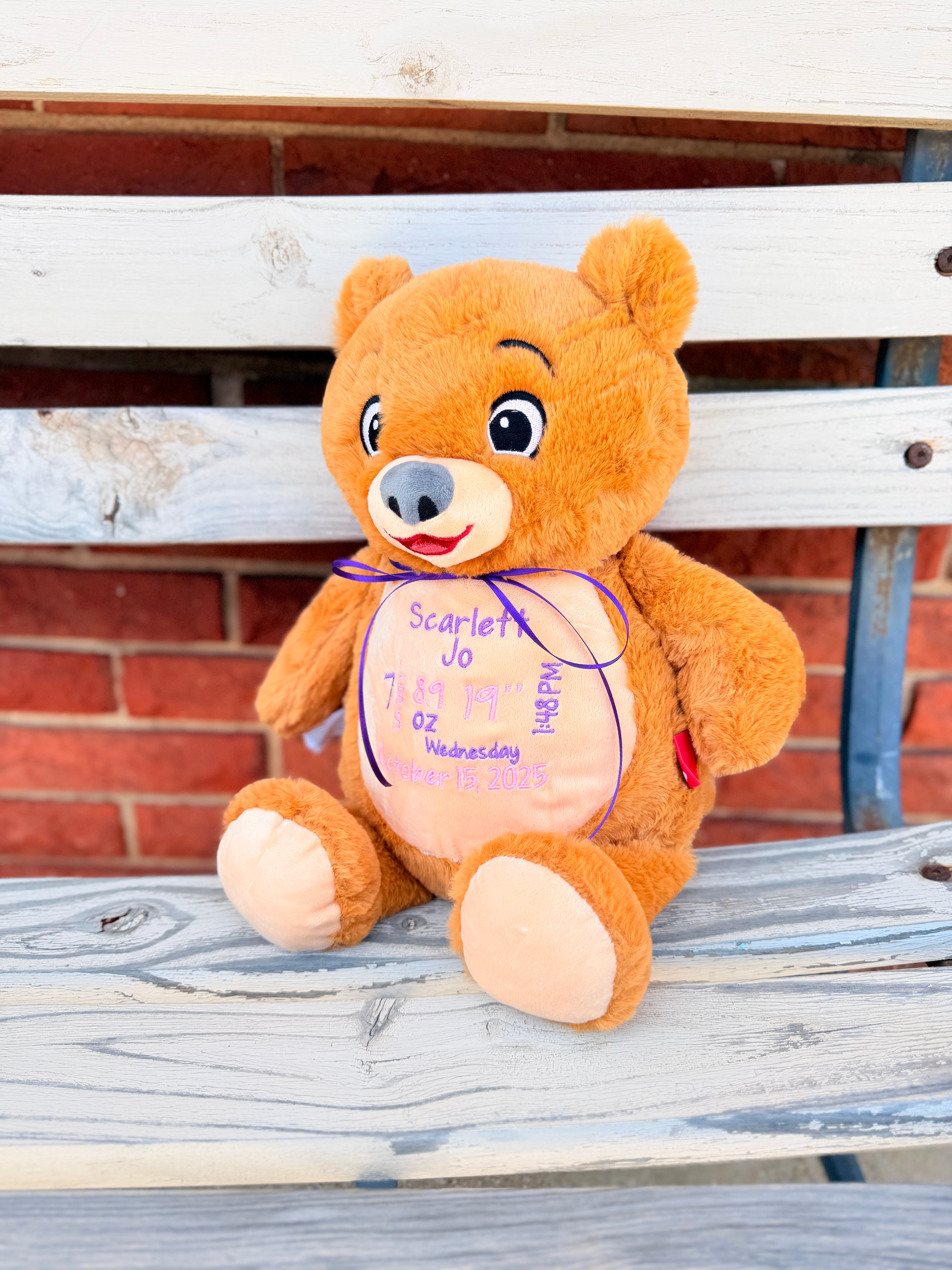 A plush teddy bear that is light brown with a tan belly embroiered with babies birth info.