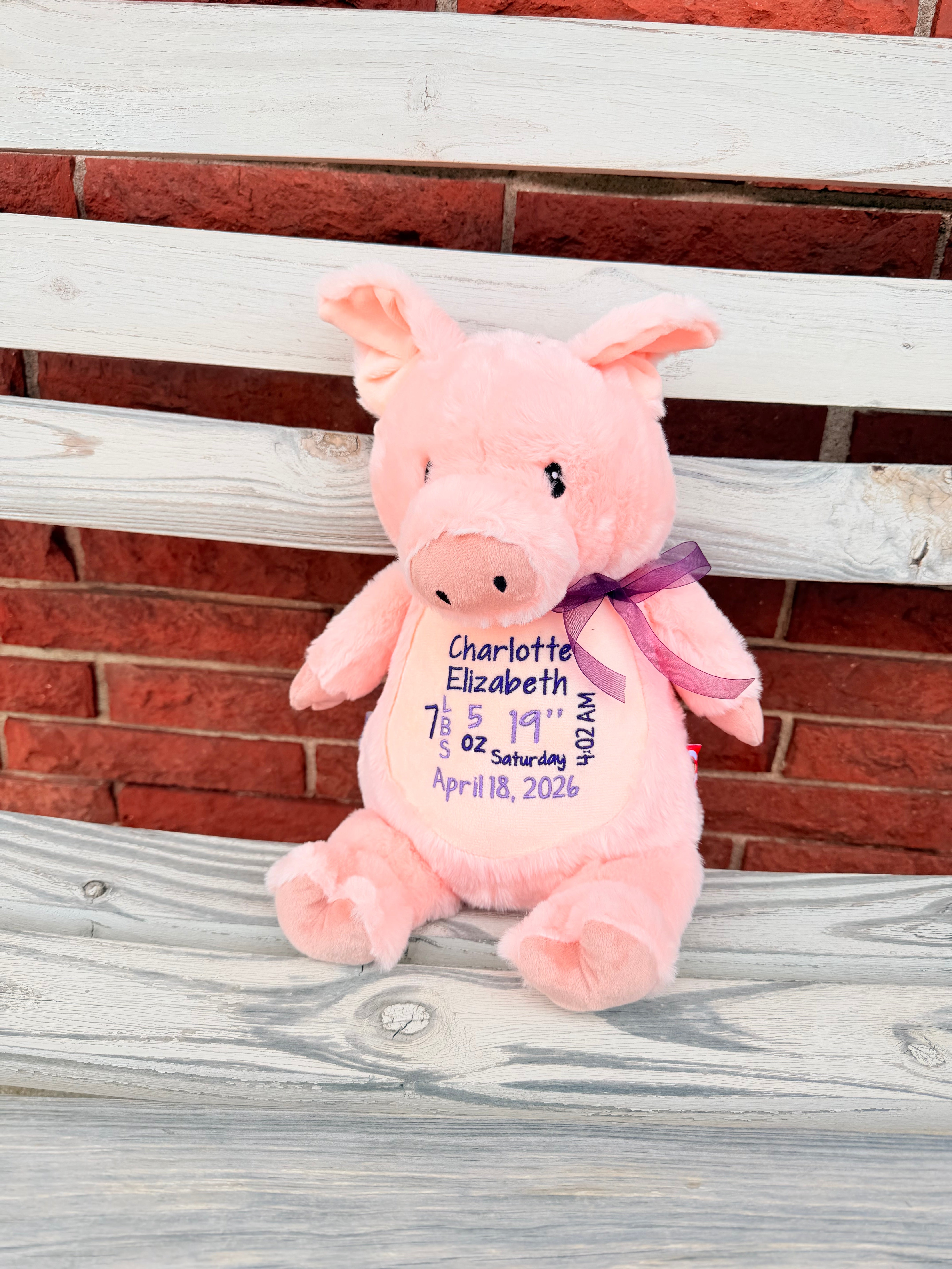 Pink plush pig with embroidered text on a wooden surface