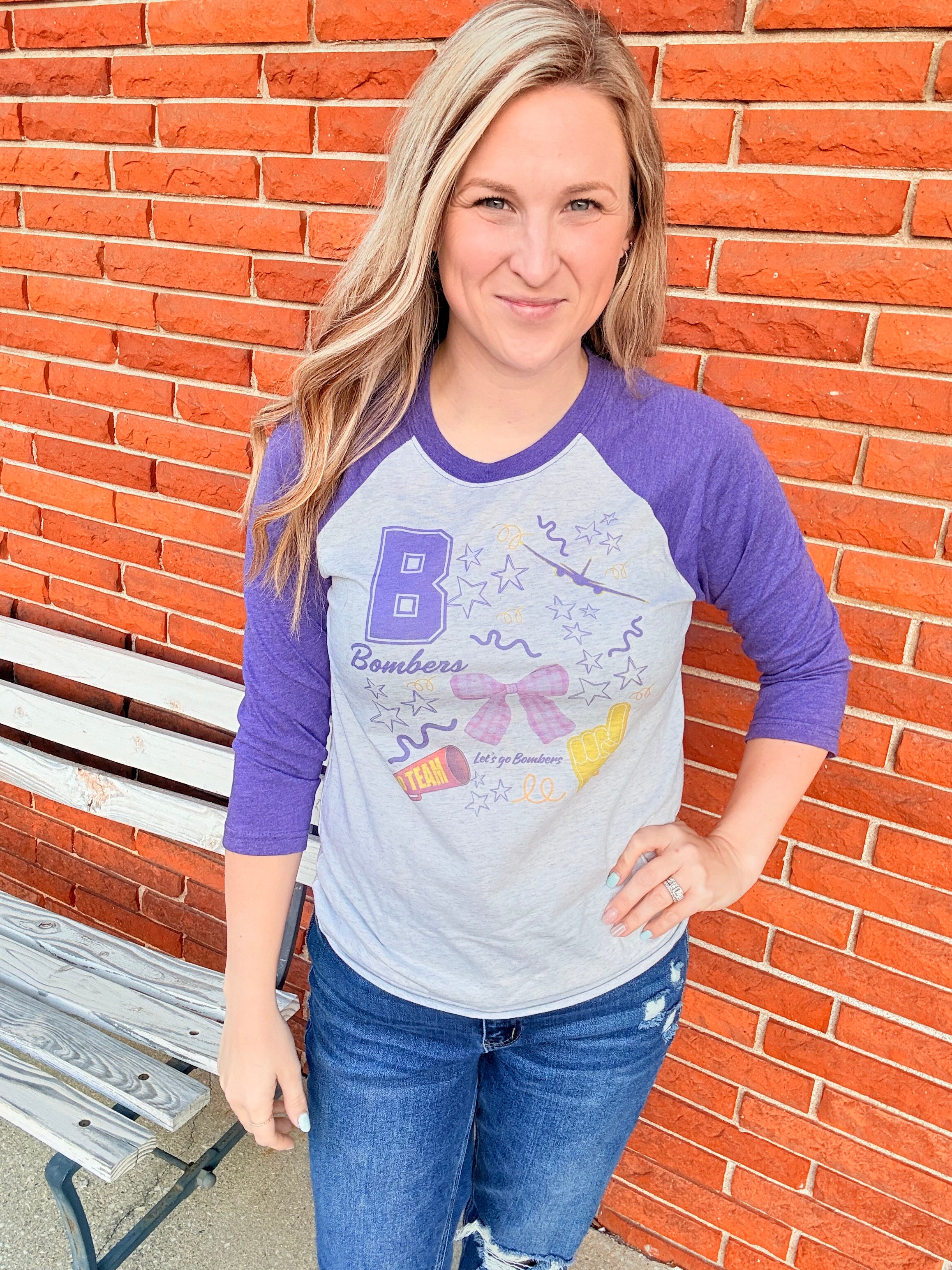 Person wearing a purple and white long-sleeve shirt with a graphic design, sitting on a brick surface.