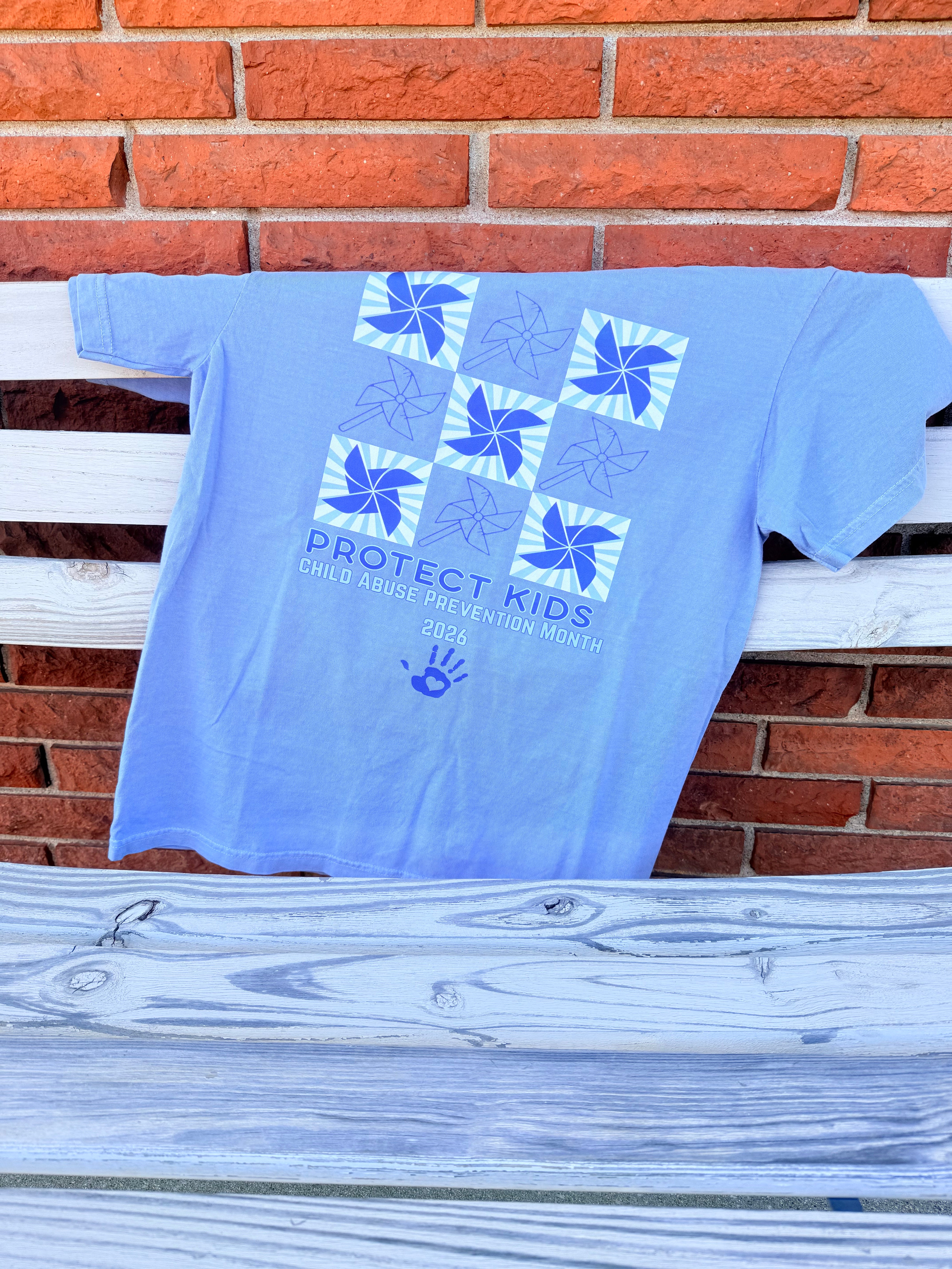 Blue sweatshirt with a logo and text hanging on a clothesline against a brick wall.