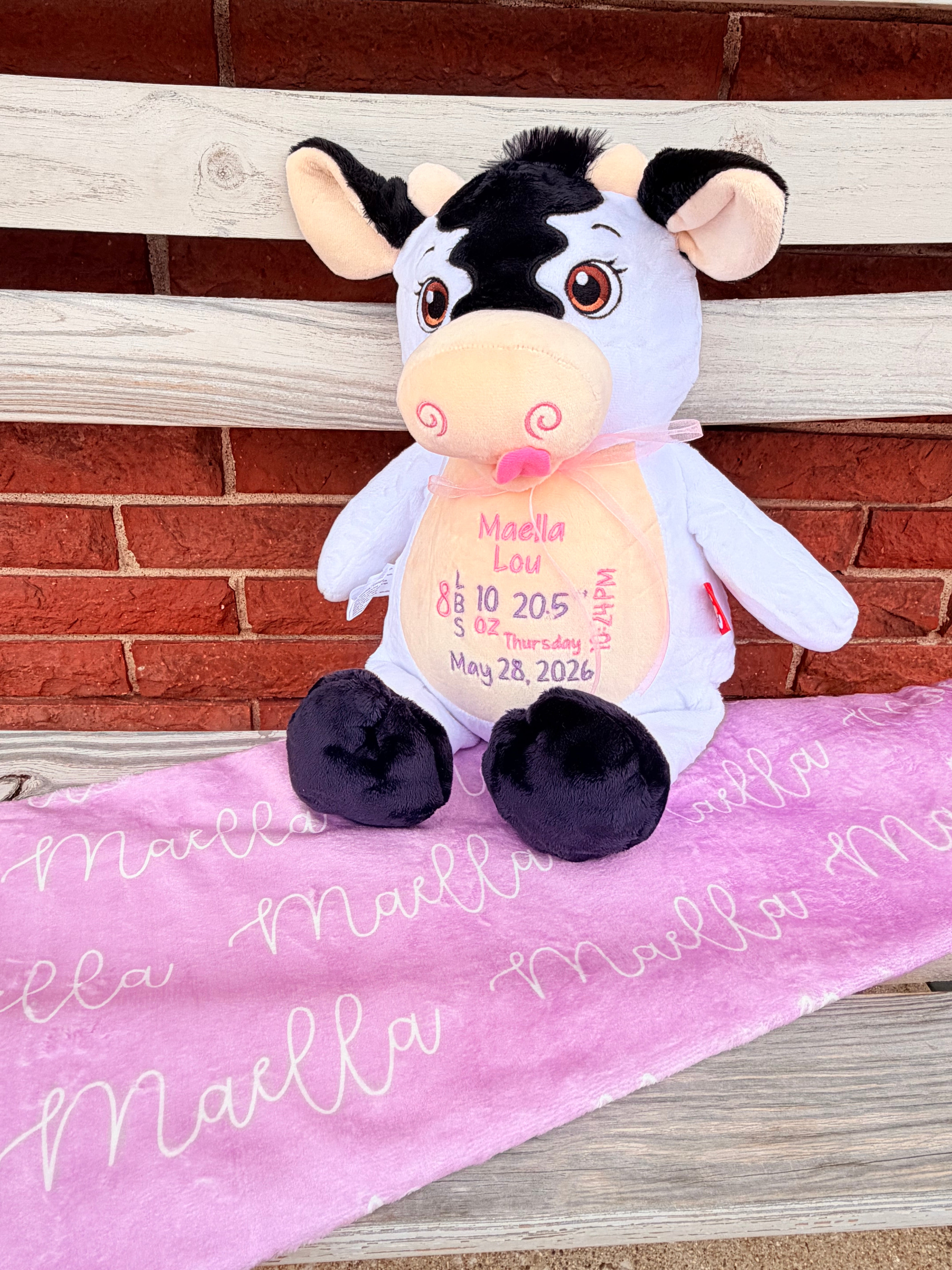 Plush cow toy with a tag on a pink blanket against a wooden background
