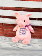 Pink plush pig with embroidered text on a wooden surface