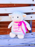 White plush lamb toy with pink ribbon and personalized text on a wooden surface