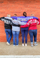 Four people wearing sweatshirt with school names against a brick wall.